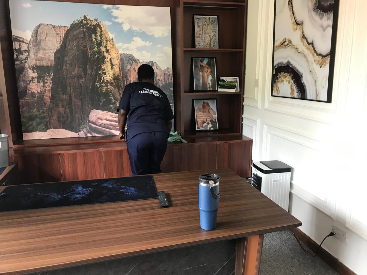 An OnyxHawk crew member in branded uniform dusting office shelving